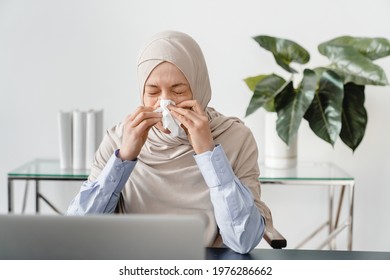 Arabian Muslim Mature Businesswoman In Hijab Sneezing At Home Office. Sick Ill Female Freelancer Feeling Unwell At Workplace. Sick Leave, Allergy, Respiratory Illness, Coronavirus Concept