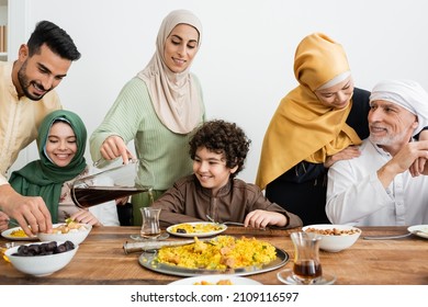 arabian woman pouring tea near happy multiethnic muslim family having dinner at home