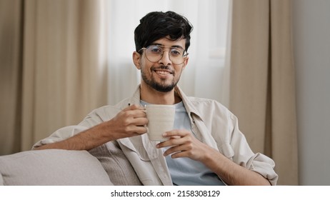 Arabic bearded millennial man latin guy in glasses sitting at home enjoying delicious hot fruit herbal tea coffee drink cocoa drinking cappuccino beverage says yes positively nod head cosiness concept