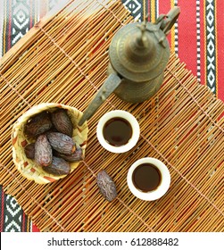 Arabic Black Coffee Served In Traditional Coffee Cups And Jug With Basket Of Dates. A Rustic Set Up From Above.