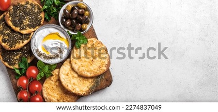 Arabic breakfast, labneh yogurt, manakeesh or pita bread with cheese and zaatar, olives and vegetables, top view, banner. Middle eastern meal, arabic cuisine.