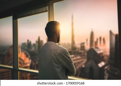 Arabic business man looking out through the office balcony seen through glass window. arab young man looking at Dubai city through hotel window. - Shutterstock ID 1700059168