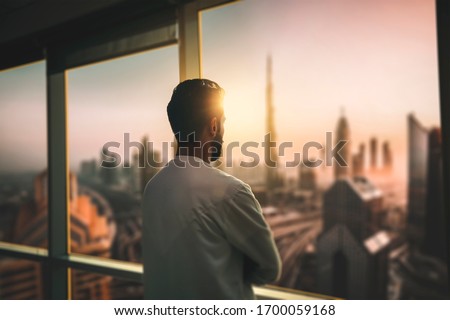 Arabic business man looking out through the office balcony seen through glass window. arab young man looking at Dubai city through hotel window.