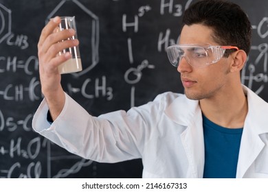 arabic chemist conducting experiment mixing liquids in flask, laboratory assistant in goggles showing chemical reaction in lesson, chemistry science concept