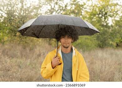 Arabic guy holding umbrella while strolling outside. He is looking at camera with true delight and sincere smile. Copy space
