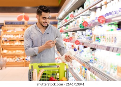 Arabic Guy Scanning Milk Bottle Using Phone Application During Grocery Shopping Standing In Modern Supermarket. Mobile Technology And Consumerism Concept