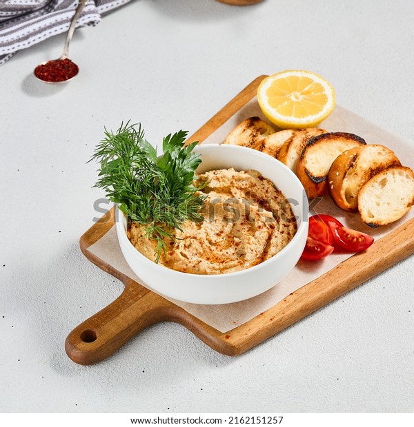 Arabic hummus with\
crispy bread and greens. Hummus dip on ceramic bowl in concrete\
background. Aesthetic composition with hummus. Arabic food.\
Oriental menu in minimal\
style