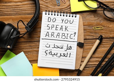 Arabic language learning with notebook question, headphones, and stationery on wooden desk