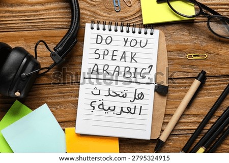 Arabic language learning with notebook question, headphones, and stationery on wooden desk