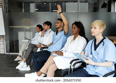 Arabic Man Doctor Raising Hand Up While Listening To Speaker, Multiethnic Group Of Doctors Attending Medical Conference Or Training At Clinic. Education And Training For Health Care Professionals