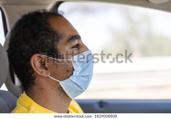 An Arabic man in\
the United Arab Emirates driving between Al Ain and Abu Dhabi\
wearing a protective face\
mask