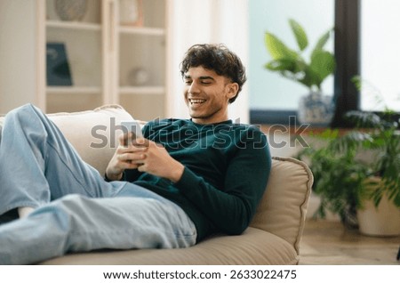 Arabic Man Using Phone Lying On Couch Relaxing At Home