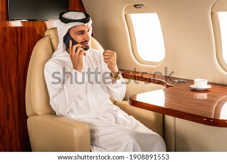 Arabic man wearing kandora in emirates style flying on exclusive private jet - Middle-eastern businessman with traditional dress flies in exclusive business class on airplane