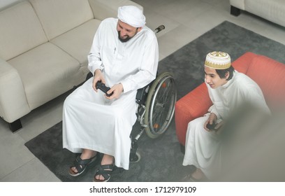 Arabic man in wheelchair at home playing video games with son