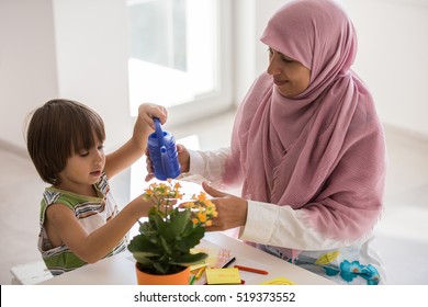 Arabic mother with little son in living room watering flowers - Shutterstock ID 519373552