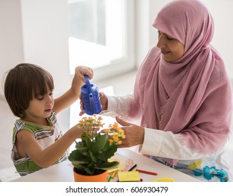 Arabic mother with little son in living room watering flowers - Shutterstock ID 606930479