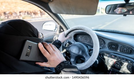 Arabic muslim woman driving a car while using her smart phone - Shutterstock ID 1490436596