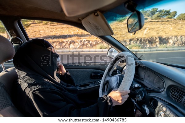 Arabic muslim woman driving a car while using her\
smart phone