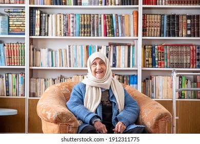 Arabic old woman sitting on couch in her home with a library background