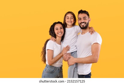 Arabic Parents And Daughter Embracing Together Posing Standing In Studio On Yellow Background, Wearing White T-Shirts. Shot Of Loving Middle Eastern Family Concept