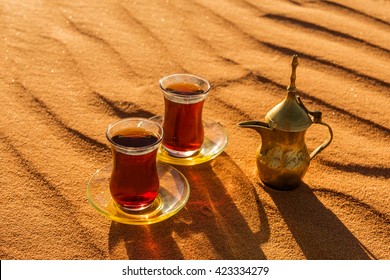 Arabic Tea In Traditional Glasses And Pot On Desert At Sunset