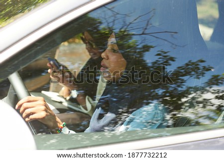 Similar – Eine Frau in einer mit großem Ausschnitt sitzt in ihrem Auto auf der rechten Seite vorne und schminkt sich, legt Schmuck an. Man kann sie durch die Reflexion in der Windschutzscheibe nicht erkennen