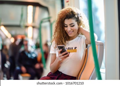 Arabic Woman Inside Subway Train Looking At Her Smart Phone. Arab Girl In Casual Clothes.