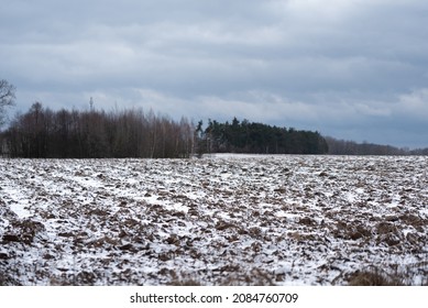 Arable fields under a thin layer of snow. Rural landscape in winter with freezing temperatures. A plowed field, prepared for the cultivation of grain.