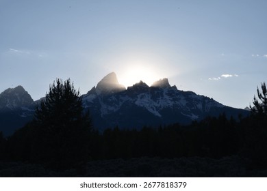 araffe mountain range with sun shining behind it and trees