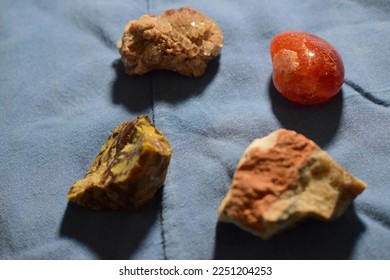 Aragonite, carnelian, industrial opal and psilomelane on pale blue background.A closeup of minerals on wrinkled fabric, studio shot.Orange, brown, red minerals.Mineralogy, geology. - Shutterstock ID 2251204253