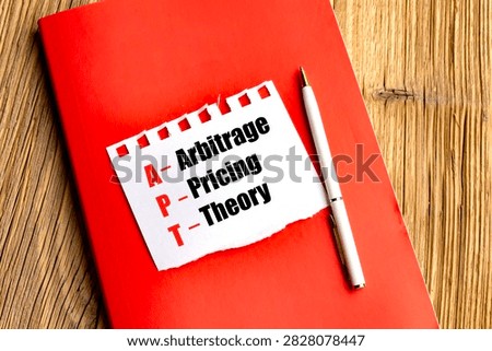 Arbitrage pricing theory concept with apt acronym on paper, red notebook and pen on wooden desk, representing finance. 