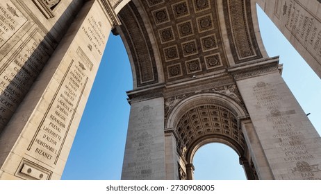 Arc de triomphe monument featuring intricate neoclassical architecture, historical engravings, and decorative details framed against a bright blue sky, representing history and national identity