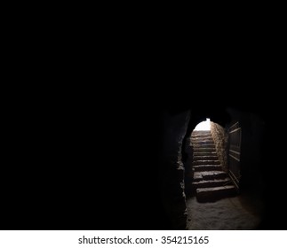 Arc fort passageway from cold damp Blackness to glow Light with rusted iron grate cell. Gaol rugged ominous shadow solid hallway with upward leading to day sunlight with space for text on sky backdrop