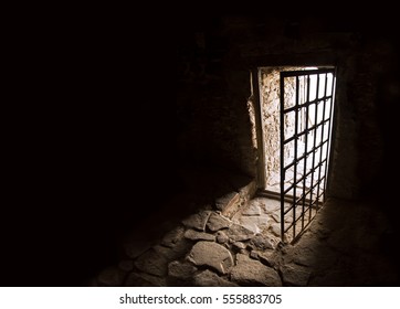 Arc fort passageway from cold damp Blackness to glow Light with rusted iron grate cell. Gaol rugged ominous shadow solid hallway with upward leading to day sunlight with space for text on sky backdrop - Shutterstock ID 555883705