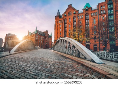 Arch bridge over alster canals with cobbled road in historical Speicherstadt of Hamburg, Germany, Europe. Scenic view of red brick building lit by golden sunset light - Powered by Shutterstock