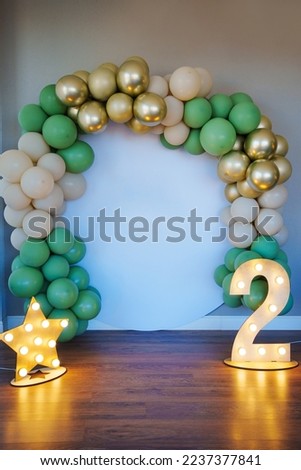 an arch of gold, green and beige balloons, lamps in the shape of a number two and a star. background for the photo shoot. Decoration of the house for the holiday. decorator services.