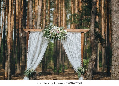 arch for the wedding ceremony, decorated with cloth flowers and greenery, is in a pine forest - Powered by Shutterstock