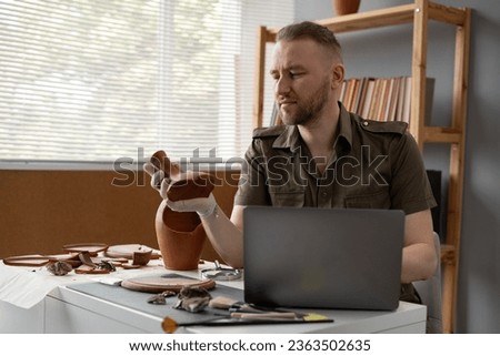 Archaeological digging. Male archaeologist doing research, using laptop computer, analysing ancient civilization culture artifacts, old vessels. Work in the office. Copy space