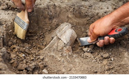 Archaeological excavations, archaeologists work, dig up an ancient clay artifact with special tools in soil - Shutterstock ID 2133470883