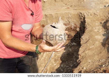 Archaeological excavations. Man's hand taking found artefact - age-damaged ceramic jar, ground work background. Real digger process. Outdoors, copy space, close up.      