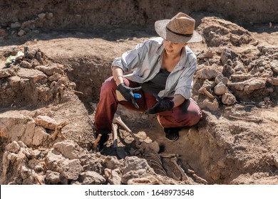 Archaeological excavations. Young archaeologist excavating part of human skeleton and skull from the ground. 