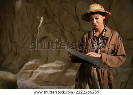 archaeologist in brown jacket and safari hat looking at ancient map in cave Foto d'archivio © 