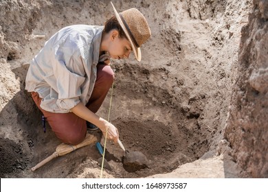 Archaeologist digging with hand trowel, recovering ancient pottery object from an archaeological site.