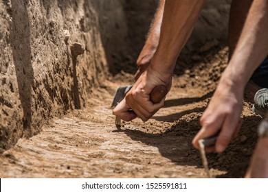Archaeologists excavating and scraping deposits with trowels
