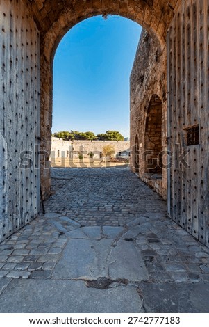 Arched gate passage inside the Castle of Pylos in Greece, with wooden doors, stone walls, and a cobblestone floor leading to the bright courtyard.