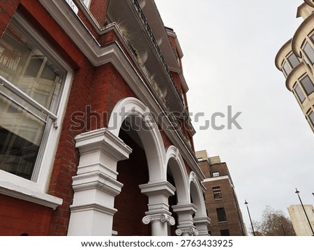 Arched redbrick facade with classical columns and balconies along a central London, UK street under overcast skies.