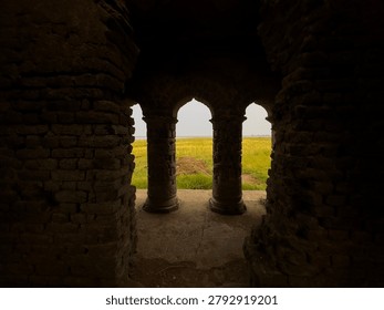 Arched stone gateway frames a bright green field with a distant horizon under a cloudy sky.
