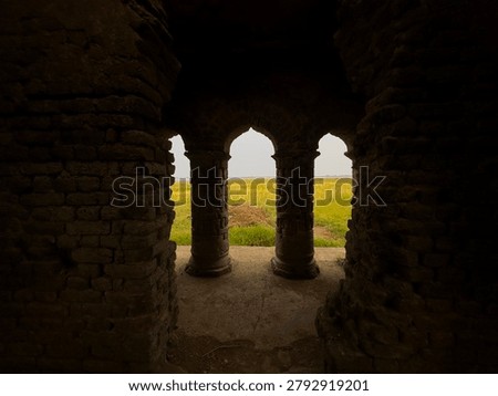 Arched stone gateway frames a bright green field with a distant horizon under a cloudy sky.