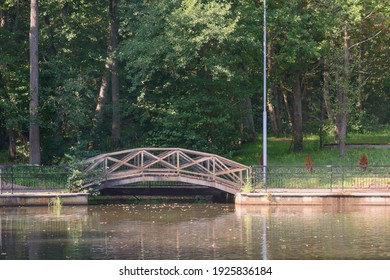 Arched wooden bridge with railing across lake in city park. 