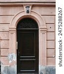  Arched wooden door in a weathered pinkish-brown stone wall, with a lantern above and intricate metalwork in the transom.